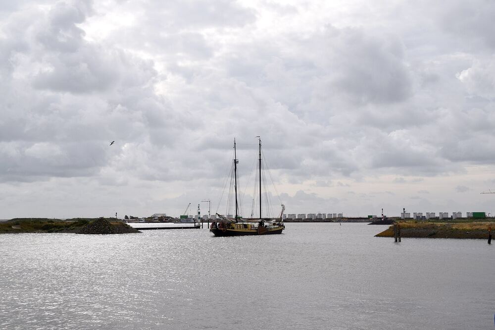 Zeilschip met twee masten vaart de haven van Den Oever uit, met op de achtergrond de sluizen van de Afsluitdijk